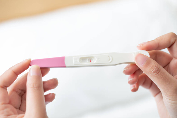 A closeup of a woman's hand holding up a pregnancy test kit with a negative result - Photo, image