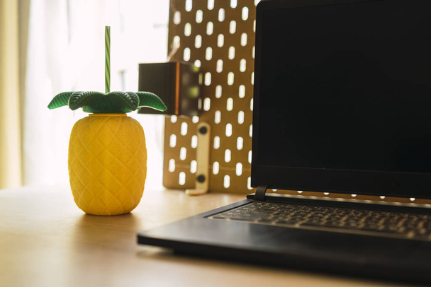 A closeup shot of a pineapple water bottle and an open laptop - Фото, изображение
