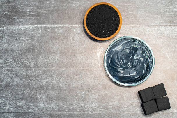 Charcoal, crushed fraction, homemade face mask and activated charcoal scrub of powder and yoghurt on white wooden background. - Fotoğraf, Görsel