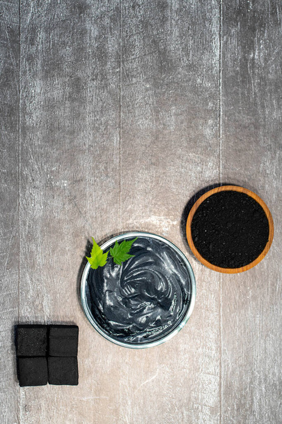 Charcoal, crushed fraction, homemade face mask and activated charcoal scrub of powder and yoghurt on white wooden background. - Φωτογραφία, εικόνα