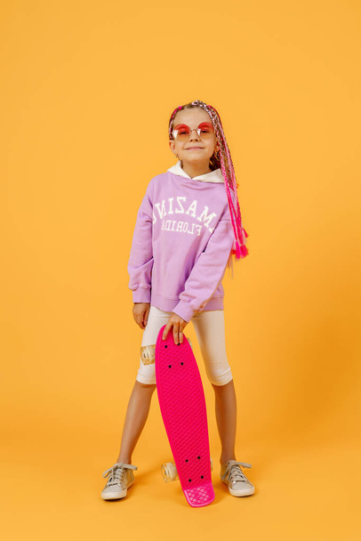 Active young girl in pink shirt and white shorts holding skatebo - Foto, Imagem