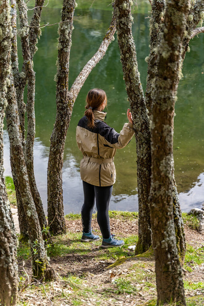 A female Caucasian hiker enjoying the quietness of the woods while standing along a riverbank - Foto, afbeelding