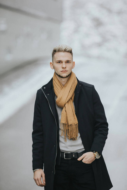 A vertical shot of a Caucasian fashionable sexy man with a brown scarf on the wall background - Foto, Imagen