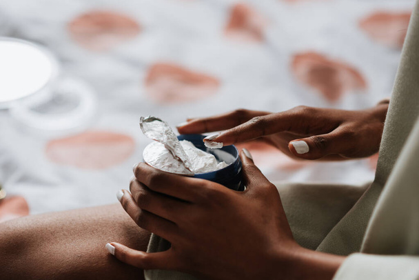 An African female holding a jar of hand cream in the bedroom - Foto, Imagem