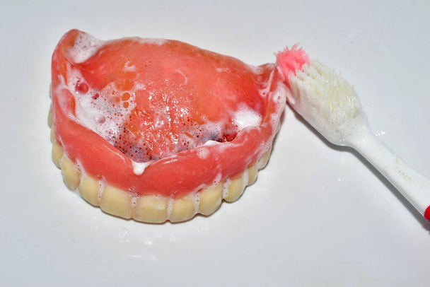 白い背景には歯磨き粉と上の入れ歯のついたブラシがあります。. - 写真・画像