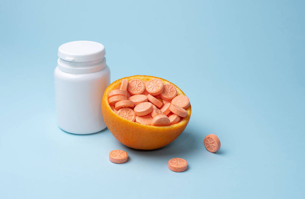 Frasco blanco y tabletas de naranja de vitamina C con media naranja sobre un fondo azul, maqueta. Concepto de refuerzo inmunológico. - Foto, imagen