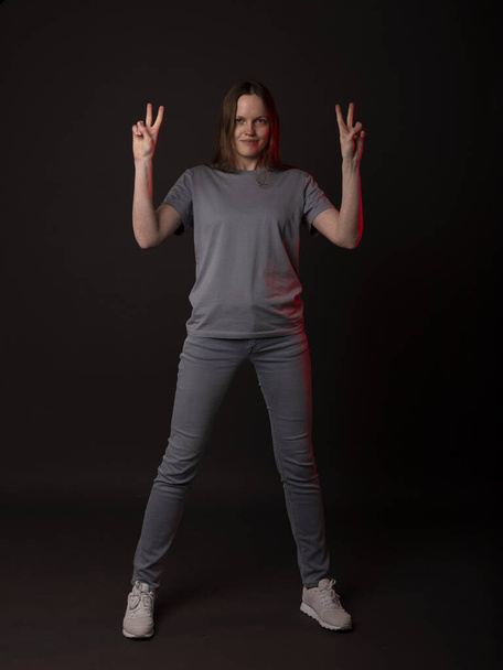 Young woman looking at camera and showing v sign or victory gesture. Person with peace fingers on black studio background - Foto, Imagem