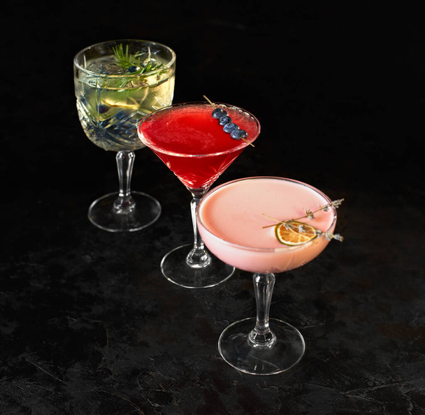 Three alcoholic cocktails stand on a black background. Iced cocktail drink with lemon and herbs. Space for text. Photo for the menu. - Фото, зображення