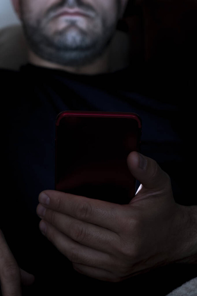 Detailní záběr muže sedícího v noci na pohovce a používajícího smartphone. Koncept nespavosti. Používání mobilních zařízení v noci - Fotografie, Obrázek