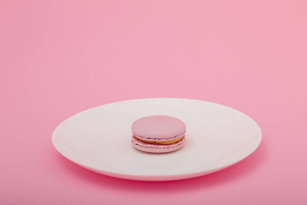 Jeden růžový makarón na bílém talíři na růžovém papíře. Sladká pekárna, kopírujte prostor. Nadváha, strava, diabetes, zdravé stravovací návyky. - Fotografie, Obrázek