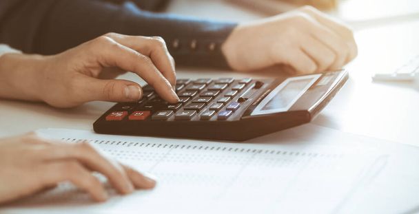 Accountant checking financial statement or counting by calculator income for tax form, hands closeup. Business woman sitting and working with colleague at the desk in office. Tax and Audit concept - Foto, afbeelding