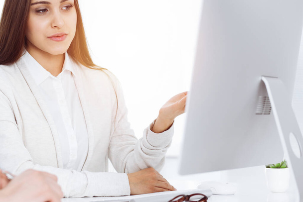 Young woman sitting at the desk with computer in sunny office. Looks like student girl or business lady communicating with casual dressed man - Foto, Bild