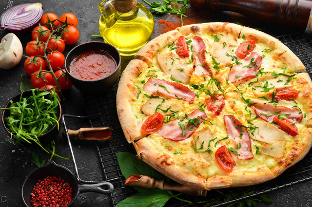 Pizza with chicken, bacon and cherry tomatoes. Italian cuisine. On a black background. - 写真・画像