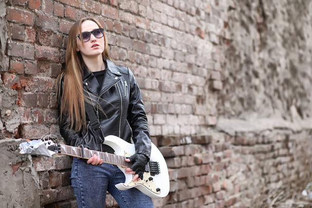  ein Rockmusikermädchen in Lederjacke mit Gitarre  - Foto, Bild