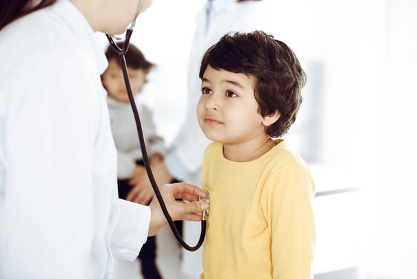 Woman-doctor examining a child patient by stethoscope. Cute arab boy at physician appointment. Medicine help concept - Foto, Imagem