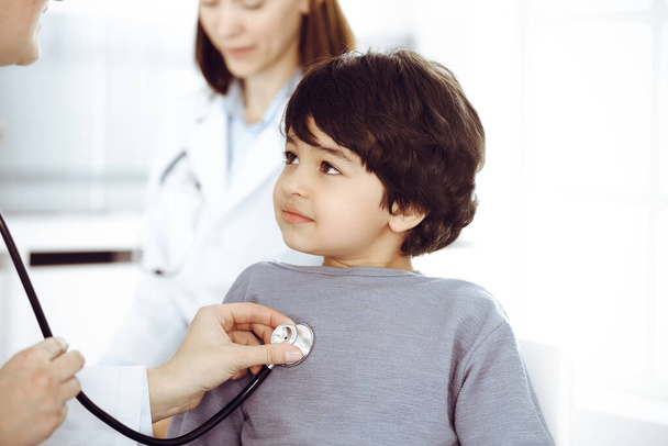 Doctor-woman examining a child patient by stethoscope. Cute arab boy at physician appointment. Medicine concept - Fotoğraf, Görsel