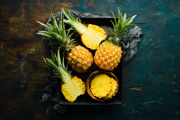 Sliced ripe baby pineapple on a black stone background. Tropical fruits. Top view. Free space for text. - Foto, imagen
