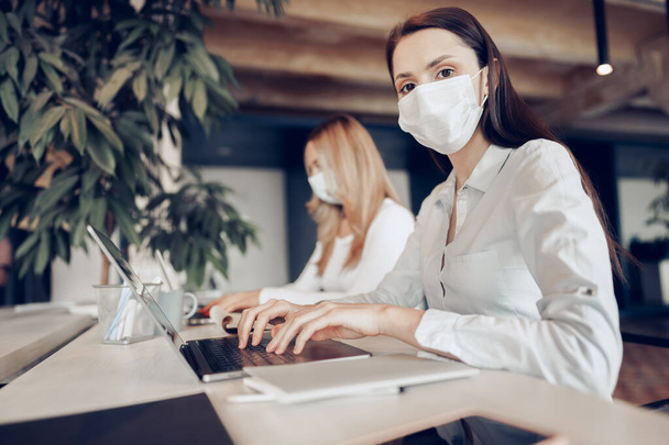 Two female colleagues working in office together wearing medical masks - Фото, изображение