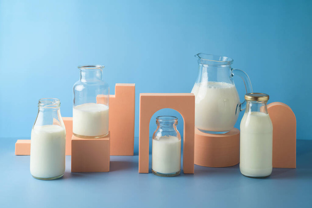 Milk bottles and milk jug over blue background. Modern still life composition. Healthy eating concept - Foto, Imagem