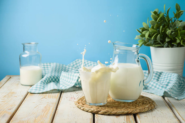 Milk glass with splash and milk jug on wooden table.  Kitchen background - Фото, изображение