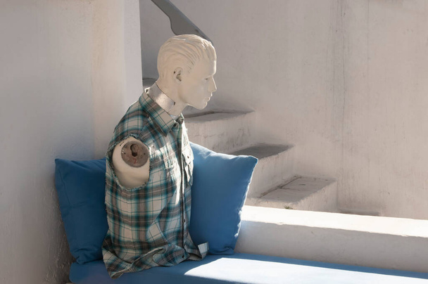 Pęknięcie bezrękiego manekina noszącego koszulę nad poduszkami, w pobliżu kamiennych schodów w wiosce na greckiej wyspie. - Zdjęcie, obraz