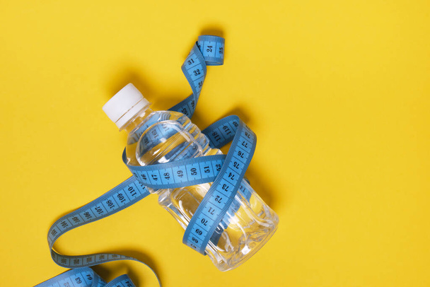 Plastic bottle of water with measuring tape on yellow background copy space top view - Fotoğraf, Görsel