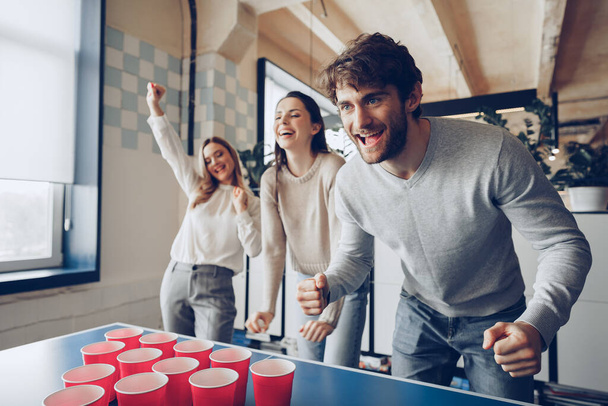 Young people coworkers playing beer pong in modern office - Foto, afbeelding