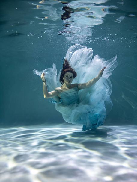   Suyun altında poz veren kırmızı saçlı, mavi elbiseli güzel bir kadın.  - Fotoğraf, Görsel