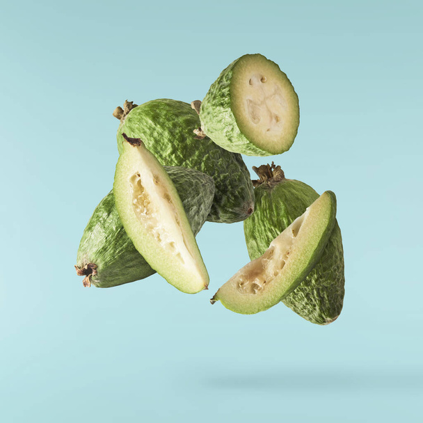 Fresh raw feijoa with green leaves falling in the air isolated on turquoise background. Food levitation or zero gravity conception. High resolution image - Photo, Image