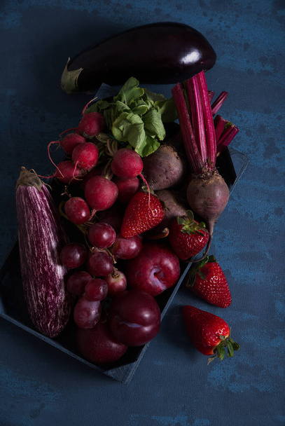 Червоні фрукти і овочі в синій дерев'яній коробці, на синьому столі
. - Фото, зображення