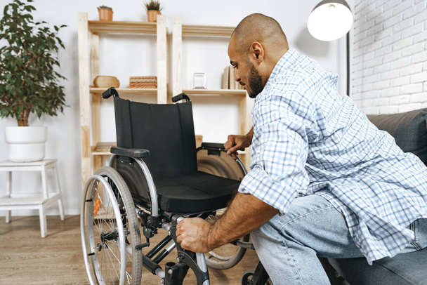 Black disabled man sits down on wheelchair at home - Foto, afbeelding