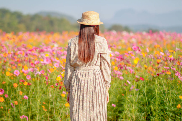The girl is praying to God with faith and the power of faith in God on the background of the morning sun rising over the fields of colorful cosmos flowers. Concepts and power of faith toward God - Foto, imagen