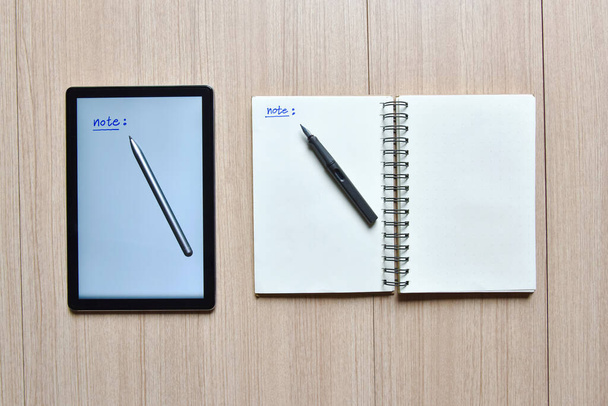 a tablet and notebook with pens on wood table,old and new style of technology to note and take a memo for note or lists concept - Photo, Image