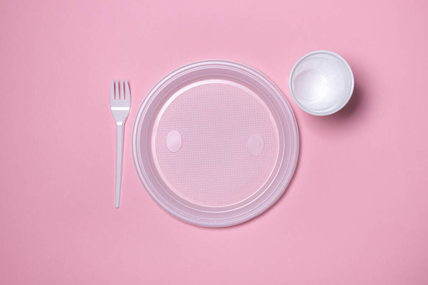 Plastic dishes on a pink background. Disposable tableware. Plastic products. - Foto, afbeelding