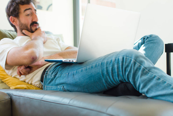 young bearded man resting on a couch with a laptop - Fotoğraf, Görsel