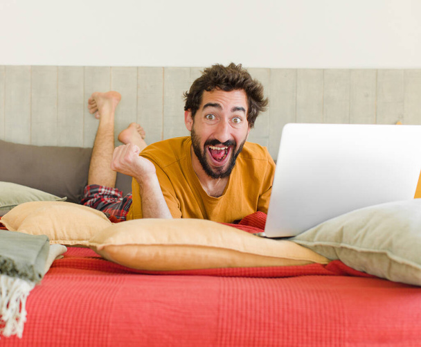 молодой бородатый мужчина на кровати с ноутбуком - Фото, изображение