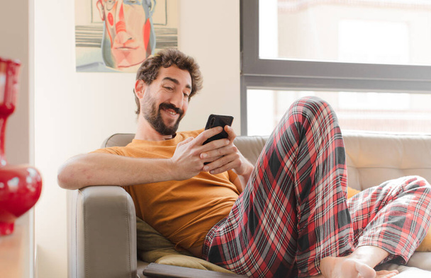 young bearded man on a couch with a smart phone - Fotografie, Obrázek