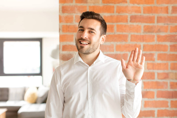 handsome businessman smiling happily and cheerfully, waving hand, welcoming and greeting you, or saying goodbye - Photo, Image