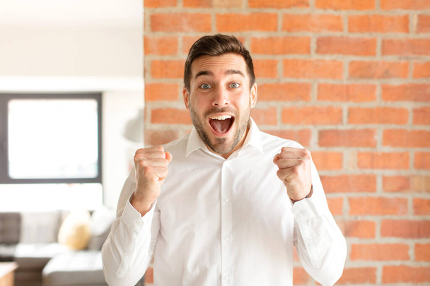 handsome businessman feeling shocked, excited and happy, laughing and celebrating success, saying wow! - Foto, afbeelding