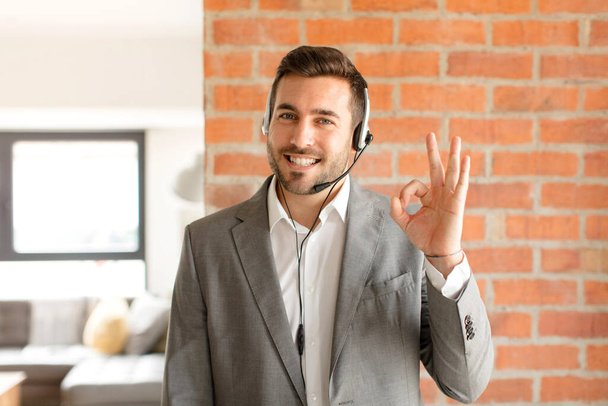 handsome telemarketer feeling happy, relaxed and satisfied, showing approval with okay gesture, smiling - Foto, Imagem