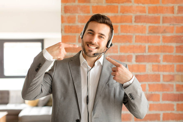 handsome telemarketer smiling confidently pointing to own broad smile, positive, relaxed, satisfied attitude - Fotoğraf, Görsel