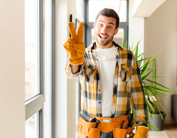 handyman smiling and looking happy, carefree and positive, gesturing victory or peace with one hand - Фото, изображение