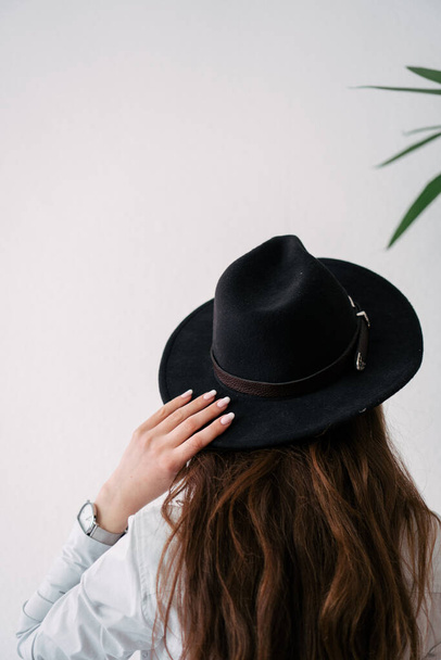 chica en un sombrero negro sobre un fondo blanco de la pared - Foto, Imagen