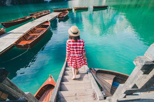 young gentle woman in red checkered dress barefoot walking by wooden stairs of boat station leads to lake. summer vacation - Фото, зображення