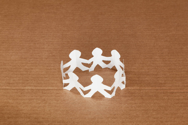Círculo de figuras humanas feitas de papel branco sobre uma superfície de papelão. - Foto, Imagem