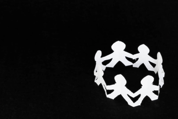Círculo de figuras humanas hechas de papel blanco sobre una superficie negra. - Foto, imagen