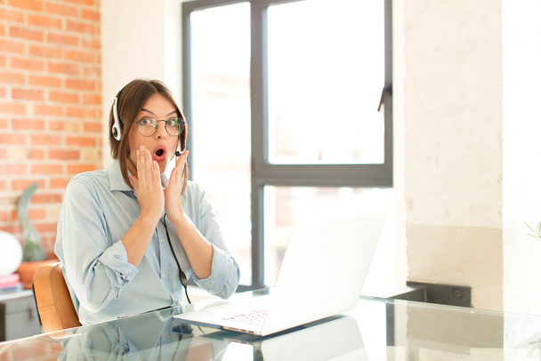 pretty telemarketer feeling shocked and scared, looking terrified with open mouth and hands on cheeks - 写真・画像