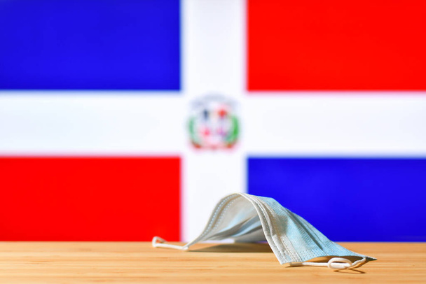 Na stole leży maska medyczna na tle flagi Dominikany. Koncepcja systemu obowiązkowej maski dla mieszkańców kraju i turystów w Republice Dominikańskiej podczas pandemii. - Zdjęcie, obraz