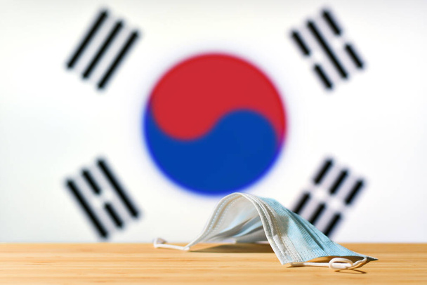 韓国の国旗を背景に医療用マスクがテーブルの上に置かれている。パンデミック時の韓国の住民と観光客のための強制マスク制度の概念. - 写真・画像
