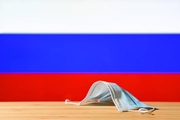 Na stole leży maska medyczna na tle flagi Rosji. Koncepcja systemu obowiązkowej maski dla mieszkańców kraju i turystów w Rosji podczas pandemii. - Zdjęcie, obraz